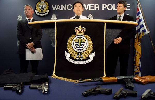 Vancouver Police Chief Jim Chu, centre, is flanked by Insp. Mike Porteous, left, and Vancouver Mayor Gregor Robinson, right, as he announces several gang-related arrests while some of the weapons seized as part of the busts are displayed in Vancouver, B.C., on Friday, March 6, 2009. (CP/Darryl Dyck)