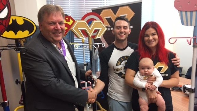 Erie St. Clair LHIN CEO Ralph Ganter receives superhero IV poles from Iain Macri and Chantelle Bacon from the Fight Like Mason Foundation (Peter Langille/AM800)