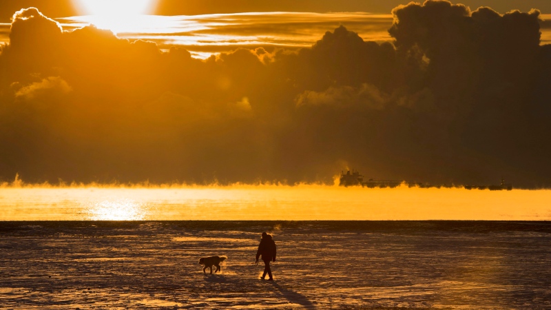 A man walks his dog across the snow-covered beach while a cargo ship sits in the steaming fog of Lake Ontario in Toronto on Dec. 27, 2017. Extreme cold temperatures have covered much of North America. (THE CANADIAN PRESS/Frank Gunn