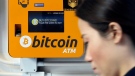 In this Dec. 21, 2017 file photo, a woman walks past the Bitcoin ATM in Hong Kong. The growth of bitcoin is fueling speculation about the environmental impact of the energy needed to power the cryptocurrency, stemming from the process of "mining," which is central to its existence. (AP / Kin Cheung, File)