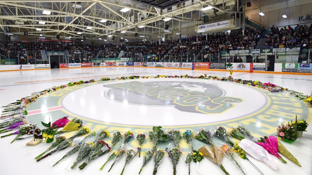Flowers lie at centre ice as people gather for a v