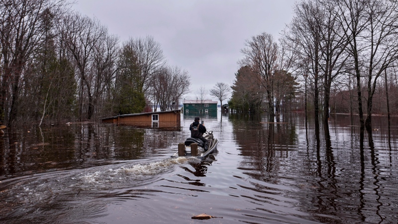 A man rides a personal watercraft in front of flooded homes on Grand Lake, N.B. as floodwaters continue to rise from the Saint John River on Tuesday, May 1, 2018. THE CANADIAN PRESS/Darren Calabrese