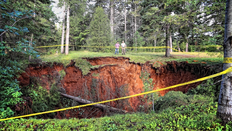 Men look at a sinkhole in Oxford, N.S. on Aug.23, 2018 in a handout photo. A Nova Scotia town is urging the public to take caution as officials scramble to assess the massive, expanding sinkhole that has sucked up surrounding trees and picnic tables. (THE CANADIAN PRESS/HO-Sean Whalen Photography)
