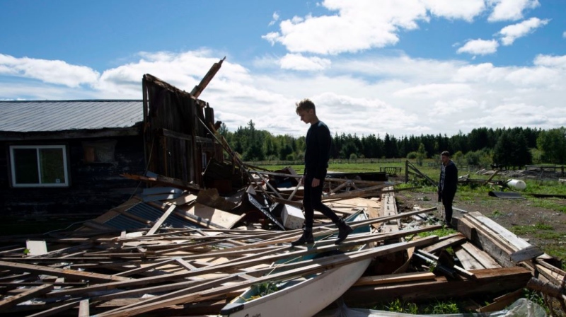Kyle Tully walks along beams from a barn that was destroyed by a tornado at his home on his cousin Christine Earle's farm, as his boyfriend Colt Webber looks on, in Dunrobin, Ont., west of Ottawa, on Saturday, Sept. 22, 2018. The storm tore roofs off of homes, overturned cars and felled power lines in the Ottawa community of Dunrobin and in Gatineau, Que. THE CANADIAN PRESS/Justin Tang