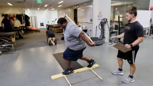 In this Oct. 8, 2018, photo, former NFL football player Vaughn Parker, left, balances himself on a plank of wood as he works with Cole Tomlinson during a range of motion and balance evaluation at Exos in Carlsbad, Calif. Parker played for the San Diego Chargers and Washington Redskins during his time in the NFL. (AP Photo/Gregory Bull)