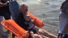 Penny Preston, 75, holds her grandson as she dips her feet into the water at Wasaga Beach as part of her 'last wish' on Tues., July 30, 2019. (CTV News/Steve Mansbridge)