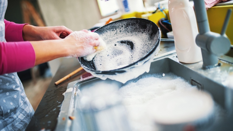 A woman washes dishes using soapy water. (iStock/Gilaxia)