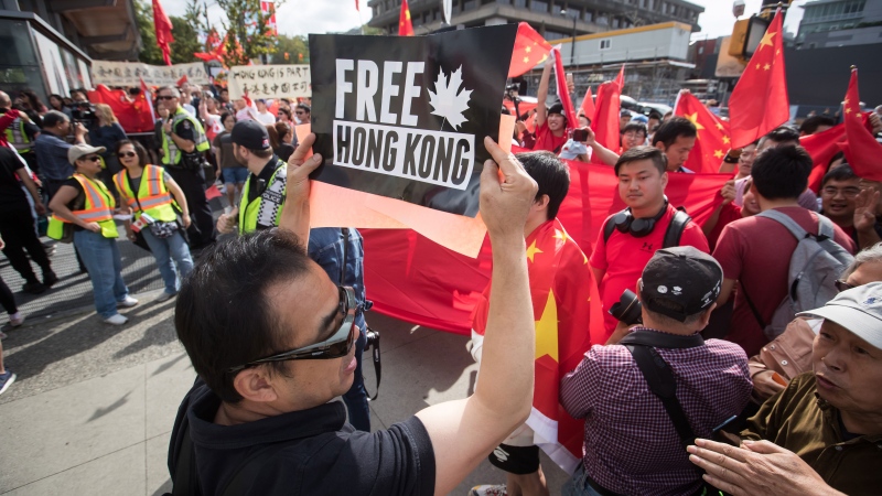 A Hong Kong anti-extradition bill protester holds up a sign in front of pro-China counter-protesters during opposing rallies in Vancouver, on Saturday August 17, 2019. THE CANADIAN PRESS/Darryl Dyck