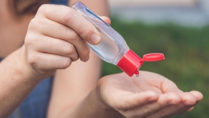 An individual uses a portable bottle of hand sanitizer outside. (Shutterstock)
