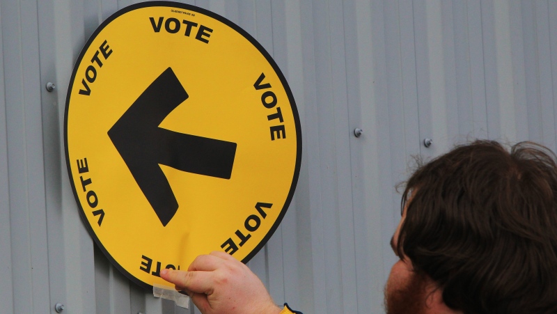 Elections Canada information officer Steven Moyer tapes a voting direction arrow sign to the Fire Hall in the village of Kerwood, Ont., Monday, Oct. 19, 2015. THE CANADIAN PRESS/Dave Chidley