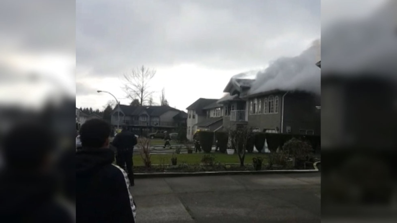 A crowd watches as smoke billows from a house fire in Surrey, B.C. on Monday, Nov. 25, 2019. 