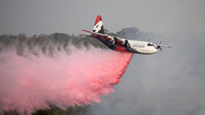 In this Jan. 10, 2020, photo, a Rural Fire Service large air tanker operated by Coulson Aviation drops fire retardant on a wildfire burning close to homes at Penrose, Australia, 165km south of Sydney. Three American crew members died Thursday when this C-130 Hercules aerial water tanker crashed while battling wildfires in southeastern Australia, officials said. (Dan Himbrechts/AAP Image via AP)