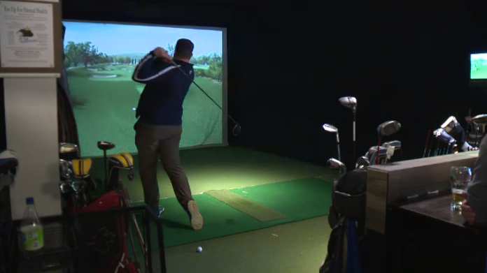 A man swings a golf club at a virtual course