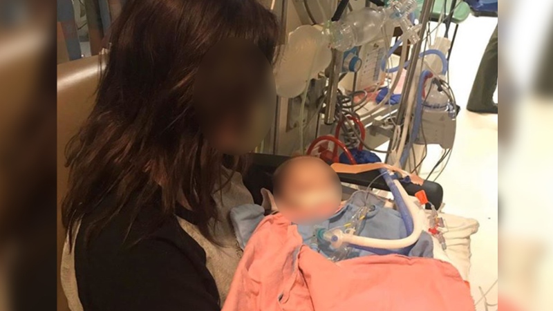 A mother holds her three-month-old baby, who later died, in hospital. The 25-year-old father is charged in the child's death.
