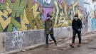 Two women wear masks as they walk down a graffiti covered alley in Toronto on Tuesday March 24, 2020. THE CANADIAN PRESS/Frank Gunn