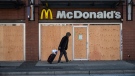 A man walks past a McDonald's restaurant with boarded up windows that has been closed due to the coronavirus, in the Downtown Eastside of Vancouver, on Wednesday, March 25, 2020. (THE CANADIAN PRESS / Darryl Dyck)