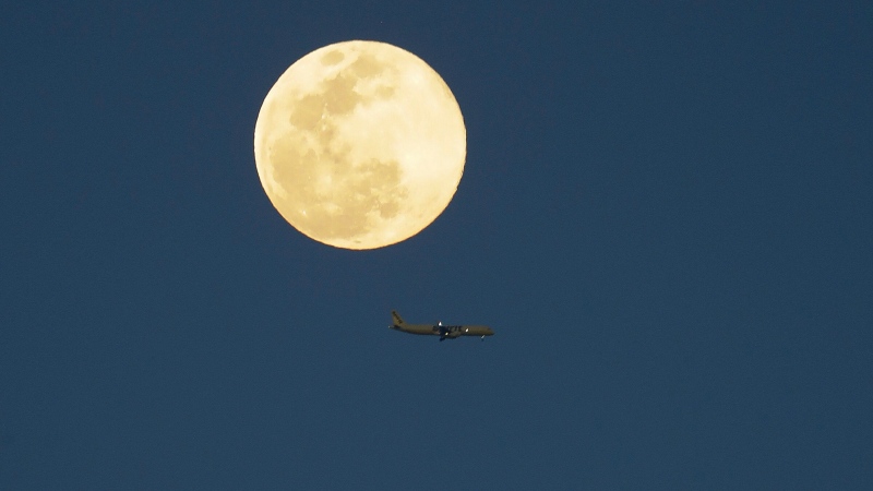 An airplane flys past a supermoon as it rises in the sky Tuesday, April 7, 2020, in Orlando, Fla. (AP Photo/John Raoux)