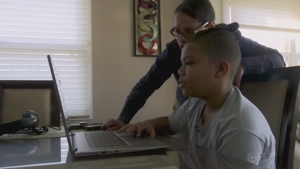 A young man does schoolwork on a laptop with his mother leaning over his shoulder. Distance learning, homeschooling and e-learning. (CTV Northern Ontario)