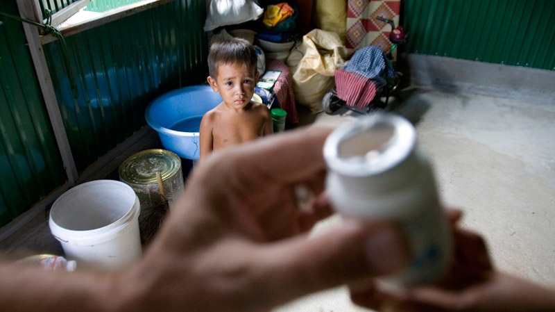 A Cambodian boy of an HIV affected family, looks on as a Cambodian medic hands over a bottle of pills to his mother in a living room at Tuol Sambo village on the outskirts of the capital, Phnom Penh, Cambodia, Friday, Aug. 28, 2009. (AP / Heng Sinith)