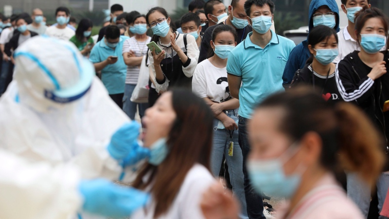 Workers line up for medical workers to take swabs for the coronavirus test at a large factory in Wuhan in central China's Hubei province Friday, May 15, 2020. (Chinatopix Via AP)