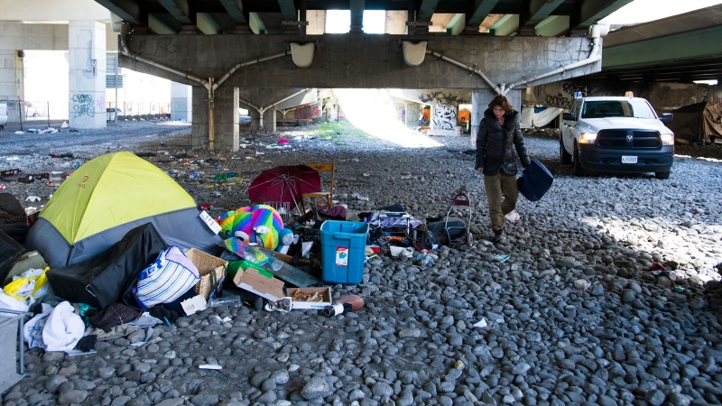 A homeless woman cleans up around her tent under the Gardiner expressway as City of Toronto workers clean up garbage during the COVID-19 pandemic in Toronto on Wednesday, May 20, 2020. THE CANADIAN PRESS/Nathan Denette
