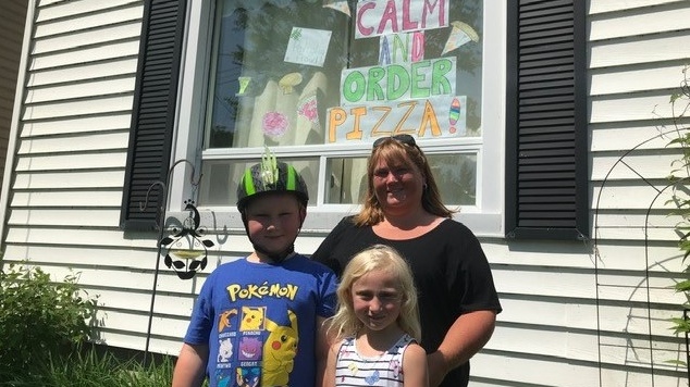 Elliott and Lila Marsden, and their mother Amy stand in front of a their window in Petrolia, Ont., one of many decorated for Petrolia’s Pizzafest this weekend, Friday, June 5, 2020. (Sean Irvine / CTV London)