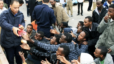 A Libyan policeman distributes bread to migrant survivors who arrived on board a rescue vessel in the port of Tripoli, Libya, on Sunday March 29, 2009. (AP) 