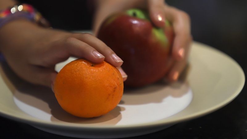 Two girls hold an orange and apple in Windsor, Ont., on Monday, June 29, 2020. (Melanie Borrelli / CTV Windsor)