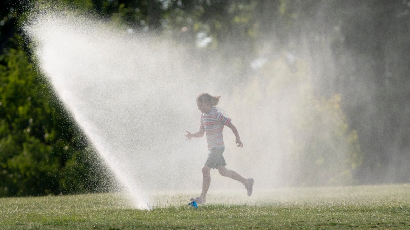 Josephine Young runs through a sprinkler as she takes a break from a bike ride near the Ottawa River on Tuesday July 7, 2020 in Ottawa. (THE CANADIAN PRESS / Adrian Wyld)