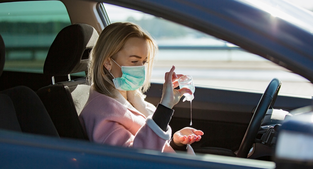 Woman wearing face mask in car using sanitizer
