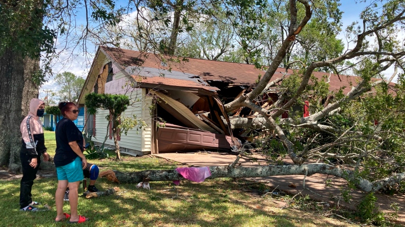 Maria Ramirez and her son 17-year old son Jose Avila stand in front of their home in Orange, Texas, Thursday, Aug. 27, 2020, and survey damage after a portion of the large tree on their front lawn was blown down onto their house by Hurricane Laura's winds. Ramirez, 57, said the tree crashed through her garage and also damaged her living room and kitchen. Ramirez said she her family had evacuated to Houston before the storm came ashore and were not at home when the tree fell. (AP Photo/Juan Lozano)