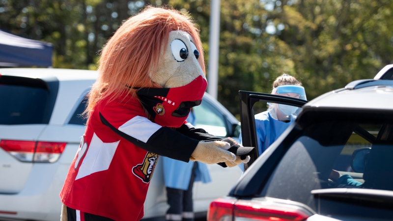 Spartacat, the official mascot of the Ottawa Senators, wears a mask as he gives a hat to a child after they received a nasal swab at a drive through, pop-up COVID-19 test centre outside the Canadian Tire Centre, home of the NHL team, in Ottawa, Sunday, Sept. 20, 2020. (Justin Tang/THE CANADIAN PRESS)