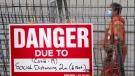 A construction sign on a fence surrounding an excavation indicates the danger of COVID-19 as a construction worker walks past Tuesday October 27, 2020 in Ottawa. (THE CANADIAN PRESS / Adrian Wyld)