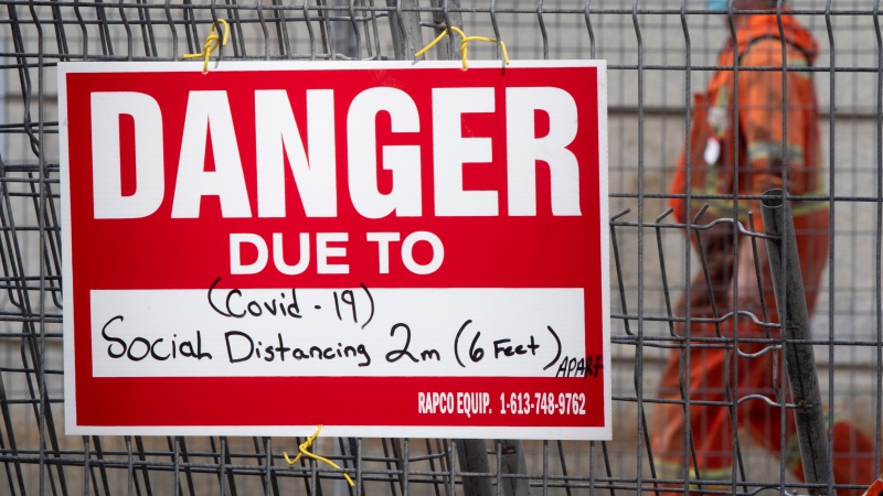 A construction sign on a fence surrounding an excavation indicates the danger is Covid-19 as a construction worker walks past Tuesday October 27, 2020 in Ottawa. THE CANADIAN PRESS/Adrian Wyld