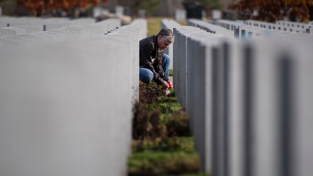 Woman lays a poppy at the grave of her husband