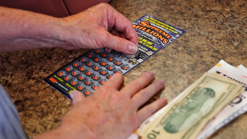 A woman scratches a $30 instant ticket while playing the lottery at Ted's Stateline Mobil on Wednesday, June 24, 2020 in Methuen, Mass. (AP Photo/Charles Krupa)
