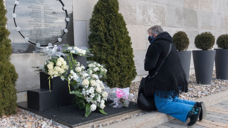 A woman kneels in front of the commemorative plaque on the wall of Polytechnique in Montreal, Sunday, Dec. 6, 2020, on the 31st anniversary of the murder of 14 women in an anti-feminist attack at Ecole Polytechnique on December 6, 1989. The COVID-19 pandemic continues in Canada and around the world. THE CANADIAN PRESS/Graham Hughes