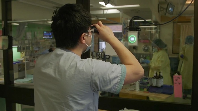 A doctor uses binoculars to look into a room in the intensive care unit of St. Paul's Hospital before deciding whether to enter. (Providence Health Care) 