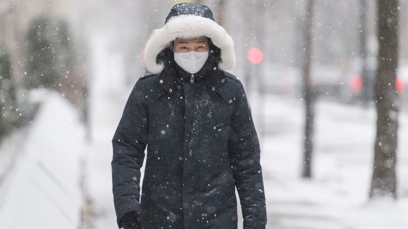 A man wears a face mask as he walks along a street during light snowfall in Montreal, Sunday, December 20, 2020 as the COVID-19 pandemic continues in Canada and around the world. THE CANADIAN PRESS/Graham Hughes