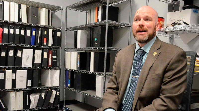 Detective Scott Marshall poses with some of the cold case files at the Battle Creek Creek Police Department on Nov. 3, 2019, in Battle Creek, Mich. Police said they solved the murder of a Battle Creek woman more than 30 years later, after a newly discovered blood sample connected a man to the fatal stabbing. But no charges will be filed because Roger Plato was killed in 1988, three days before Gayle Barrus' body was found by hunters in Calhoun County, prosecutor David Gilbert said. (Trace Christenson/Battle Creek Enquirer via AP)