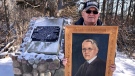 Jim Crane holds a portrait of his uncle, Dr. James Crane in front of a cairn in Dr. Crane’s memory at the site of a wooded area he donated for conservation in Elgin County, Ont., Tuesday, Feb. 2, 2021. (Sean Irvine / CTV News)