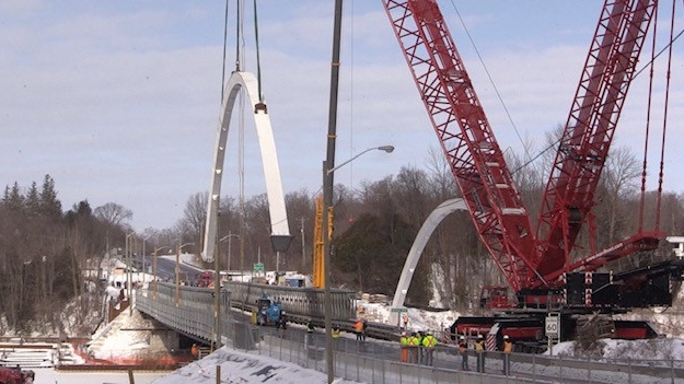 People watch as cranes lift arches for a new bridge in Bayfield, Ont. on Thursday, Feb. 11, 2021. (Scott Miller / CTV News)