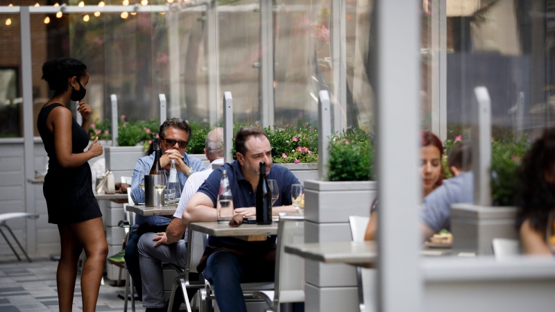 A waiter talks with patrons at a patio in Yorkville in Toronto, on Friday, June 26, 2020. THE CANADIAN PRESS/Cole Burston