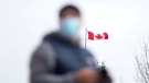 The Canadian flag flaps behind a man wearing a face mask in Montreal, Sunday, April 4, 2021. THE CANADIAN PRESS/Graham Hughes