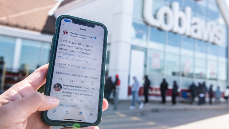 A post from Twitter account Vaccine Hunters Canada that shared details of a walk-in COVID-19 vaccination clinic at a Loblaws pharmacy in Ottawa is seen on a mobile phone as people line up outside the store, some waiting hours before the store's opening time, on Monday, April 26, 2021. (Justin Tang/THE CANADIAN PRESS)