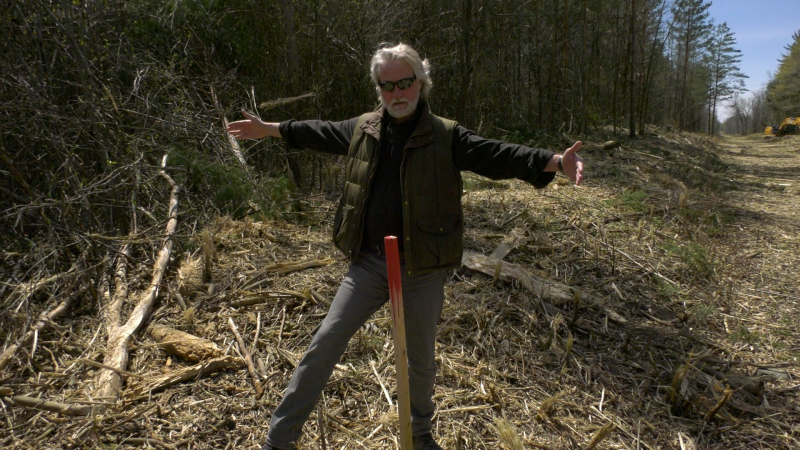Bruce Kennedy standing by a stake in the ground approximately 6 feet off the Peanut Line trail, showing cutting that was done far past the 6 foot mark. (Nate Vandermeer / CTV News Ottawa)