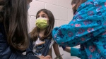 In this Wednesday, March 24, 2021 image from video provided by Duke Health, Alejandra Gerardo, 9, looks up to her mom, Dr. Susanna Naggie, as she gets the first of two Pfizer COVID-19 vaccinations during a clinical trial for children at Duke Health in Durham, N.C. (Shawn Rocco/Duke Health via AP)