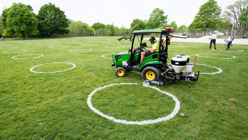 A worker paints environmentally-friendly physical distancing circles at Trinity Bellwoods Park during the COVID-19 pandemic in Toronto on Thursday, May 28, 2020. THE CANADIAN PRESS/Nathan Denette