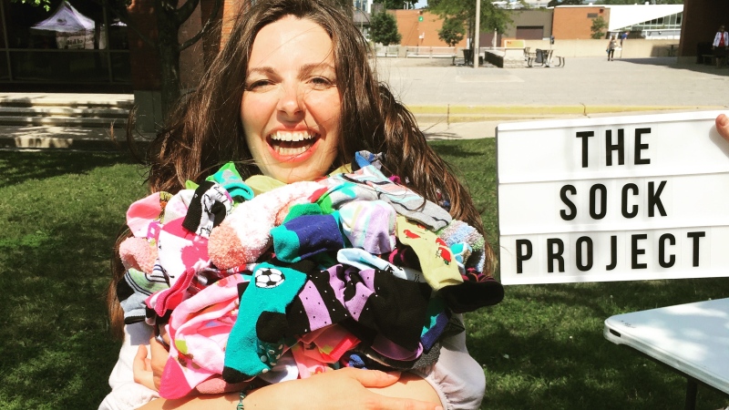 Jessica Baird poses with a pile of socks. The Sock Project gives pairs of funny and silly socks away for free to people suffering from chronic illnesses. (Photo courtesy of Jessica Baird/The Sock Project)