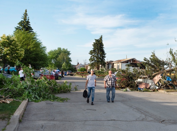 People walk past debris after a tornado touched down in Mascouche, Que., northeast of Montreal, Monday, June 21, 2021. Dozens of homes were damaged and one death has been confirmed. THE CANADIAN PRESS/Ryan Remiorz 